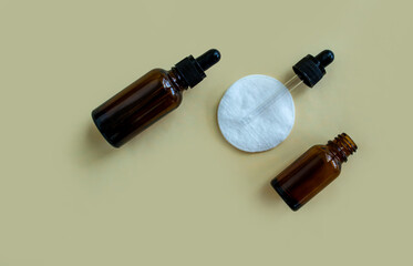 Flat lay vials with a pipette and a white cotton pad on a beige background.