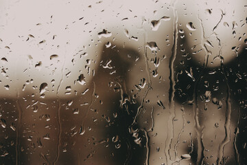 Raindrops on window creating a moody atmosphere. Close-up rain on a window, blurring the outside world. Soft sepia tones add to the tranquil feeling.
