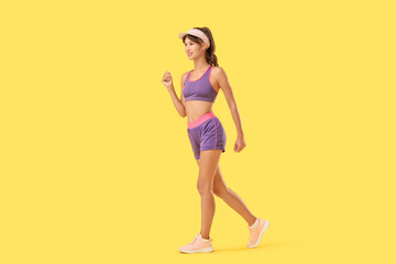 Sporty young woman walking on yellow background