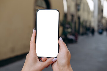Mockup woman's hand holding using smart phone with white blank screen POV at on the background of a house on the street in Europe real estate rent, mobile app design and advertising, online marketing