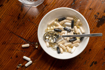 Assorted dietary supplements in a bowl with a spoon beside a glass of sparkling water on a wooden table,  health and wellness lifestyle