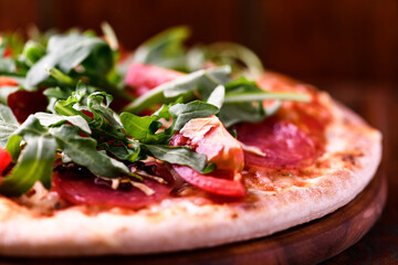 Pizza with salami, tomatoes and mozzarella cheese. Rustic wooden background. Soft focus. Copy space.	