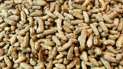 Large pile of peanuts in their shells. The texture of the rough, light-brown shells is the main focus, showing the characteristic creases, bumps, and varying shapes of the pods.