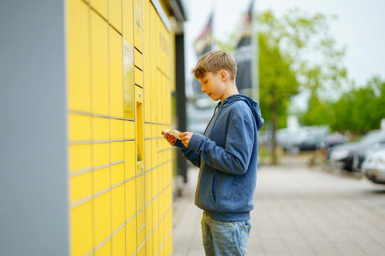 Blond boy holding ticket standing in front of parcel locker at footpath