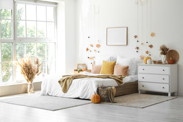 Interior of light bedroom with autumn leaves, pumpkins and commode