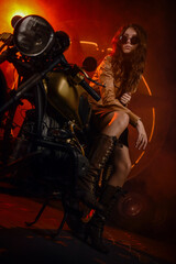 Beautiful young girl a motobiker on motorcycle in leather jacket on industrial background with smoke and round light.
