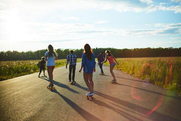 Group of teenagers skateboarding on open road during sunset, moving away from camera, enjoying outdoor activity together, casting long shadows on pavement