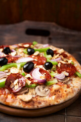 Pizza with chorizo ​​sausage, mozzarella cheese, green pepper and black olives. Rustic wooden background. Soft focus.	