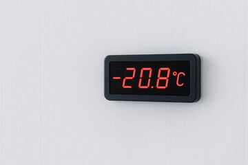 Digital wall thermometer displaying minus twenty degrees celsius in bright red numbers against a clean white wall background