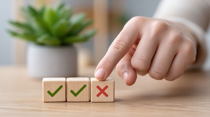 A hand points at three wooden blocks, two marked with check marks and one with a cross, alongside a decorative green plant.