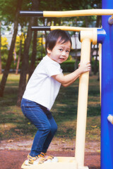 Obraz premium Little boy playing happily on a playground in the park. Kid play on outdoor Fitness Equipment in Park for Exercise. Waist-tightening exercise equipment, a child's curiosity. Baby aged 2-3 year old.