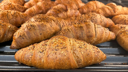 Freshly baked croissants sprinkled with sesame and flax seeds on a bakery rack. A delicious breakfast and bakery product.