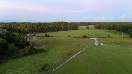 Aerial drone view of Florida farmland with green pastures, small farm structures, and a country road leading into the horizon, capturing the quiet simplicity of rural landscapes.