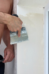 Caucasian plasterer man with a spatula applying finishing putty on a window opening