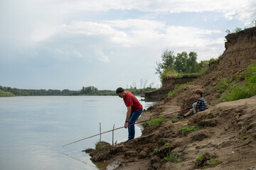 Fototapeta premium Grandfather is teaching a grandson fishing on the river beach.