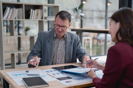Senior business manager and young business consultant working together reviewing financial reports and pointing at charts and data in office meeting