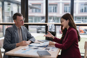Asian businesswoman pointing at financial charts and graphs showing positive growth of company to her senior male colleague while discussing new project at office meeting