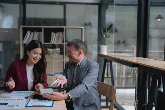 Two business colleagues reviewing financial data and using a calculator in a modern office, collaborating on a project and analyzing charts and graphs to make informed decisions