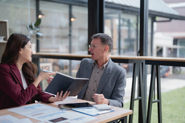 Fototapeta premium Two business people are discussing during a meeting, analyzing financial charts and data to improve their business strategy in a modern office
