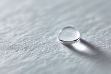 A pristine water droplet rests on a textured white surface, symbolizing purity, clarity, and condensation. Great for wellness, beauty, science or nature themes.