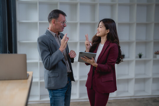 Two business colleagues, a man and a woman, are using sign language to communicate during a work meeting, enhancing accessibility and inclusion in the workplace