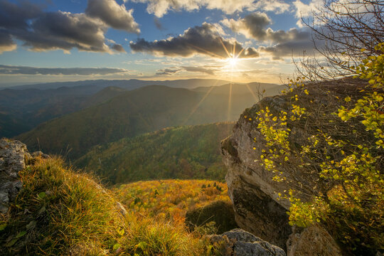 View of the sun bursting through the clouds over rolling hills dotted with autumn colors, seen from a rocky outcrop, Majerova skala rock, Star&Atilde;&copy; Hory, Banskobystrick&Atilde;&frac12; kraj, Slovakia.