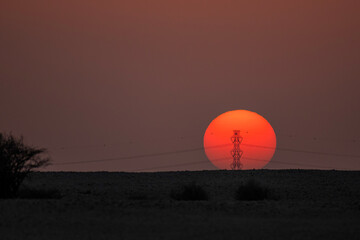 Doha, Qatar - September 7, 2025: Power transmission line poles against the sun. Sunset view with high tension pole 