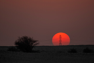 Doha, Qatar - September 7, 2025: Power transmission line poles against the sun. Sunset view with high tension pole 