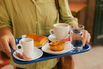 Close up middle age woman tries Portuguese egg tart pastry called Pastel de Nata with coffee near bakery in Lisbon. Solo tourism and travel. Part of a series