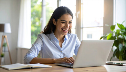 Smiling young businesswoman enjoying a successful remote job, happily typing on a laptop computer while working from her modern home office