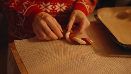 Woman Twisting Red and White Dough Strands into Candy Cane Shape on Parchment Paper, Close Up, Festive Cookie Crafting Concept