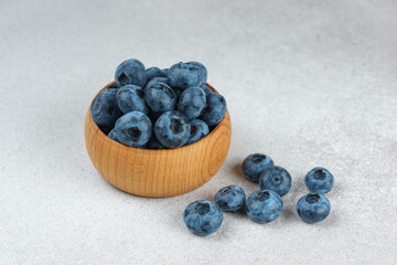 Fresh ripe blueberries in small wooden bowl on gray textured stone background. Delicious organic fruit rich in vitamins, wild berries,healthy lifestyle, natural food. Close up, macro