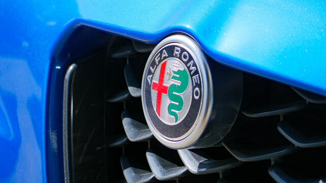 The classic Alfa Romeo logo on the iconic triangular 'Scudetto' grille of a blue car The historic emblem with the biscione serpent and cross is a symbol of Italian style and racing heritage
