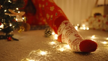 Close Up of Foot in Red and White Christmas Socks with Glowing Fairy Lights on Carpet in Warm Room, Low Angle, Cozy Holiday Detail Concept