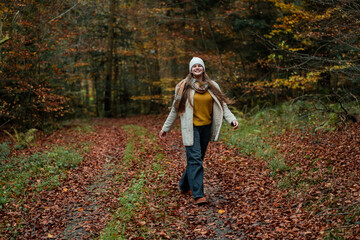 Portrait of a happy teenage girl in a hat and warm clothes on a walk in the autumn forest. Meditation and relaxation in nature.