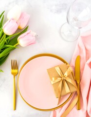Elegant, pastel-toned table setting with tulips, gift, and gold flatware