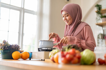 Muslim woman happy cooking healthy meal in kitchen wearing hijab making soup in pot with fresh vegetables food preparation activity nutrition, ramadan healthy recipe preparation, islamic food culture
