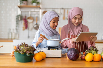 Muslim girl cooking with woman using tablet for recipe, halal food learning with technology, warm islamic family lifestyle, digital nutrition education for muslim kid, modern halal kitchen inspiration