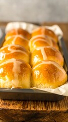 Freshly baked hot cross buns in a pan, glazed with a golden icing