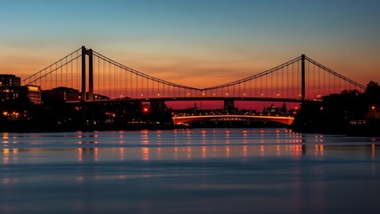 Silhouetted suspension bridge at dusk with city lights