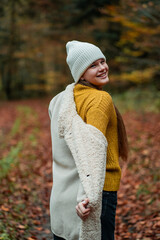 Portrait of a happy teenage girl in a hat and warm clothes on a walk in the autumn forest....