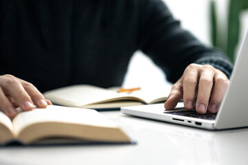 Closeup image of a male writing notes in his notebook while using laptop. Boy working on new project
