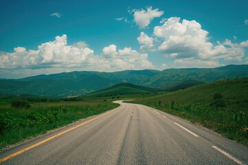 Naklejka premium Paved road winding through lush green hills under a cloudy sky