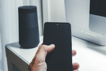 Smartphone in hand. Speaker, router, computer on desk. Technology, domotics, home automation concept