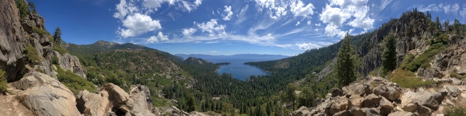 Scenic vista reveals a blue lake cradled by forested mountains, under a sky of scattered clouds and rocky terrain in the foreground