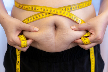 Close-up of woman squeezing abdominal fat with both hands. Concept of body fat, weight loss, fitness, and healthy lifestyle