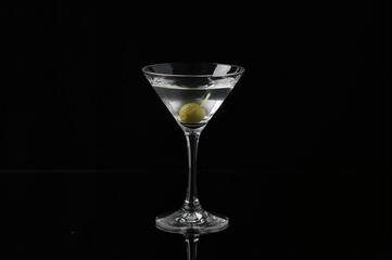 Transparent spirit in a crystal glass with an olive on a dark backdrop