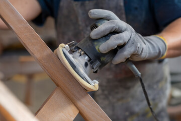 Skilled worker sands a piece of wooden furniture. Care, precision, and manual skill in artisanal woodworking. Passion for the craft and design.