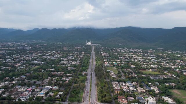 Cinematic drone video moving directly toward the majestic Faisal Mosque in Islamabad suburbs, surrounded by Margalla hills.