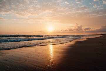 Obraz premium A breathtaking evening sky illuminates the sea, bathing the waves and coast in a warm golden light. The sunâ€™s gleam dances on the moist beach sand.